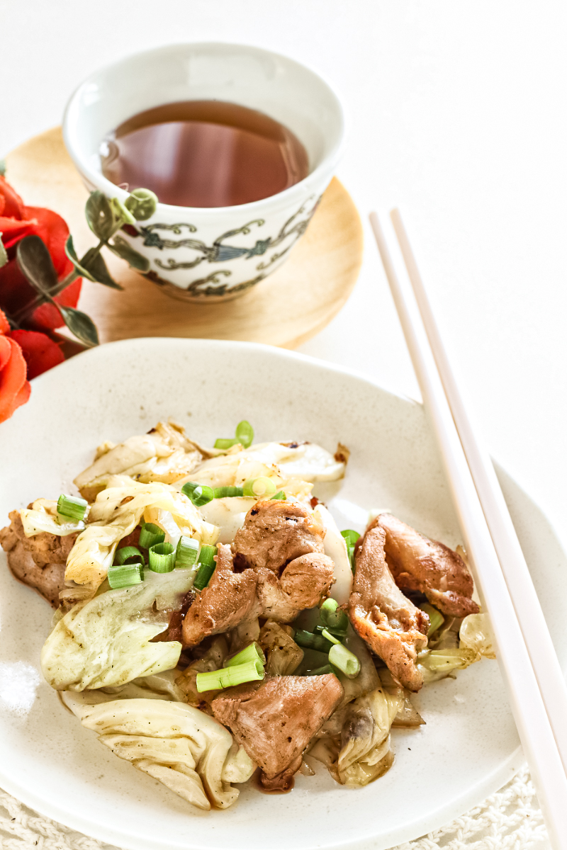 Korean chicken and cabbage skillet with garlic soy sauce, sautéed cabbage, and green onions served on a white plate with chopsticks and tea — quick high-protein chicken cabbage stir-fry.