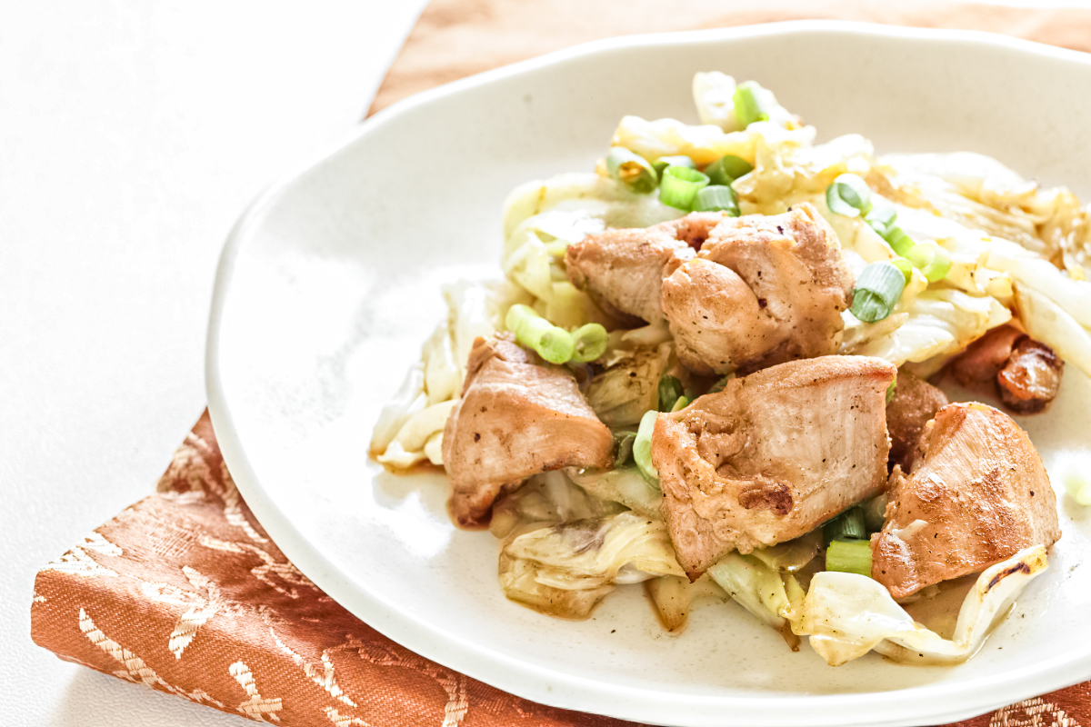 Pan-seared chicken pieces with sautéed cabbage and garlic, topped with fresh chopped green onions and served in a shallow bowl on a rustic cloth napkin for a simple weeknight skillet meal.