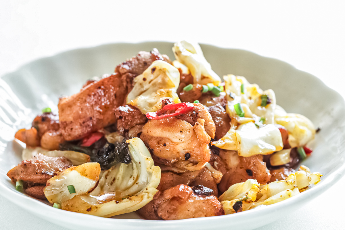 Skillet-cooked Korean-style chicken with caramelized cabbage, garlic, and sliced red chili peppers, finished with chopped green onions and served in a shallow bowl for a simple, savory weeknight meal.