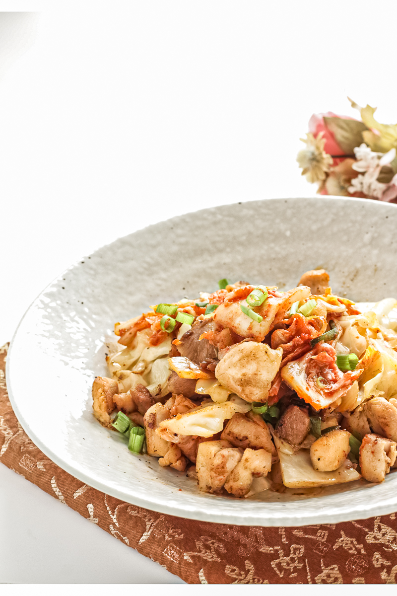 Spicy Korean chicken and cabbage skillet with kimchi, garlic, and green onions served on a white plate — flavorful kimchi chicken stir-fry variation with cabbage.