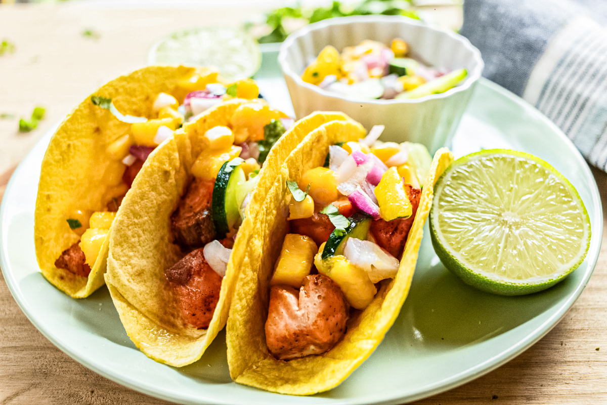 Pan-seared salmon tacos with cucumber mango salsa served in corn tortillas with lime wedges and fresh salsa on the side.
