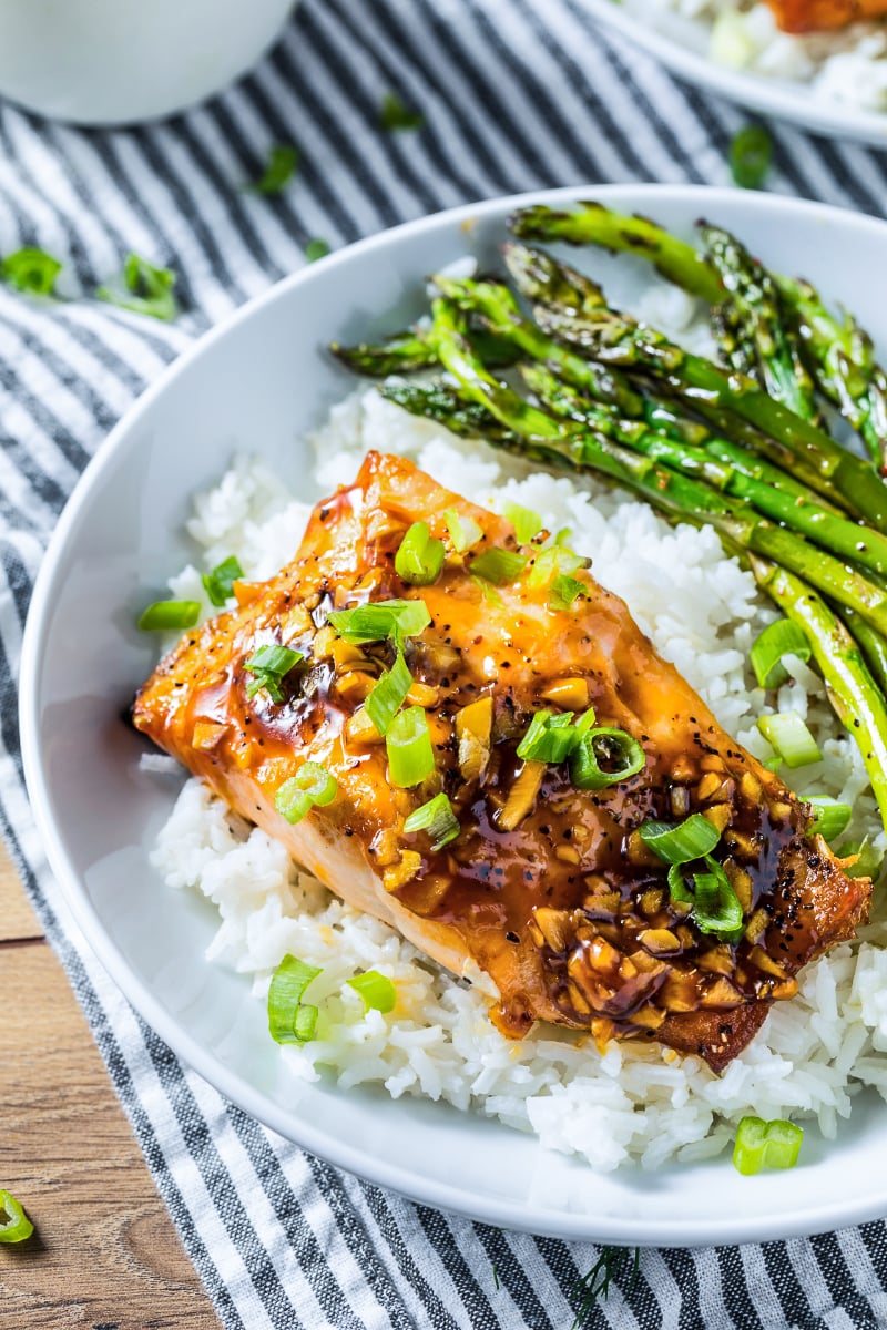 Baked teriyaki salmon with garlic glaze served over steamed white rice with roasted asparagus and sliced green onions, plated in a bowl for an easy homemade salmon dinner.