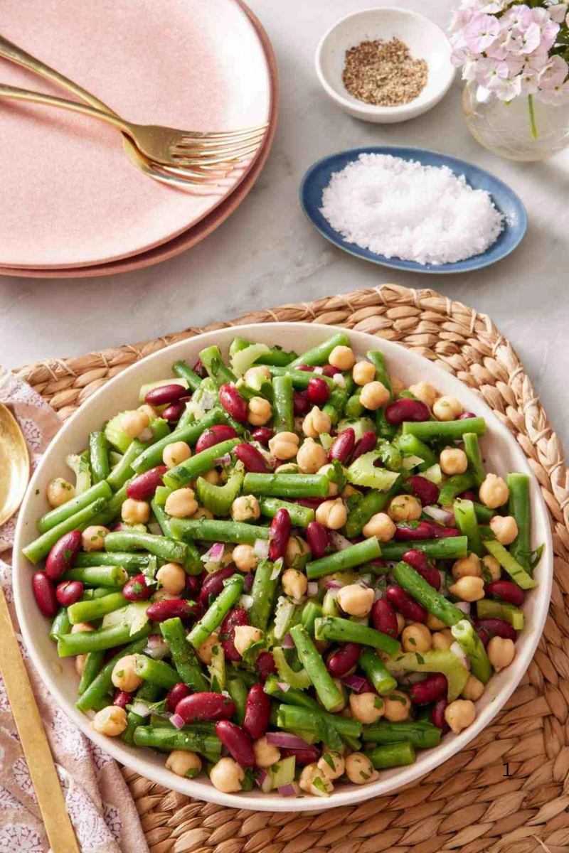 Fresh 3 Bean Salad with green beans, kidney beans, chickpeas, celery, and red onion in a serving bowl on a woven placemat