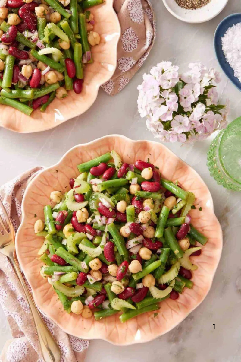 Two plates of 3 Bean Salad with green beans, kidney beans, chickpeas, celery, and red onion served on a light table setting