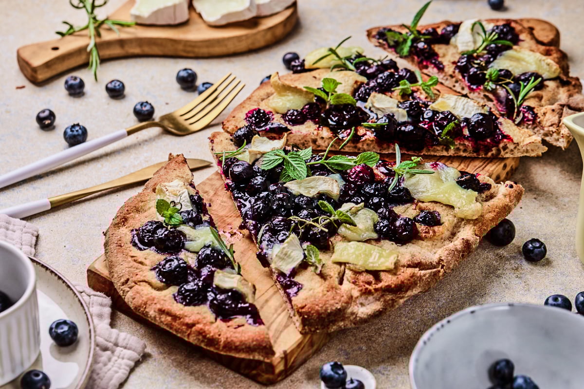 Blueberry goat cheese flatbread sliced on a wooden board with juicy baked blueberries, melted goat cheese, fresh herbs, and a crisp golden crust for a sweet-savory appetizer.