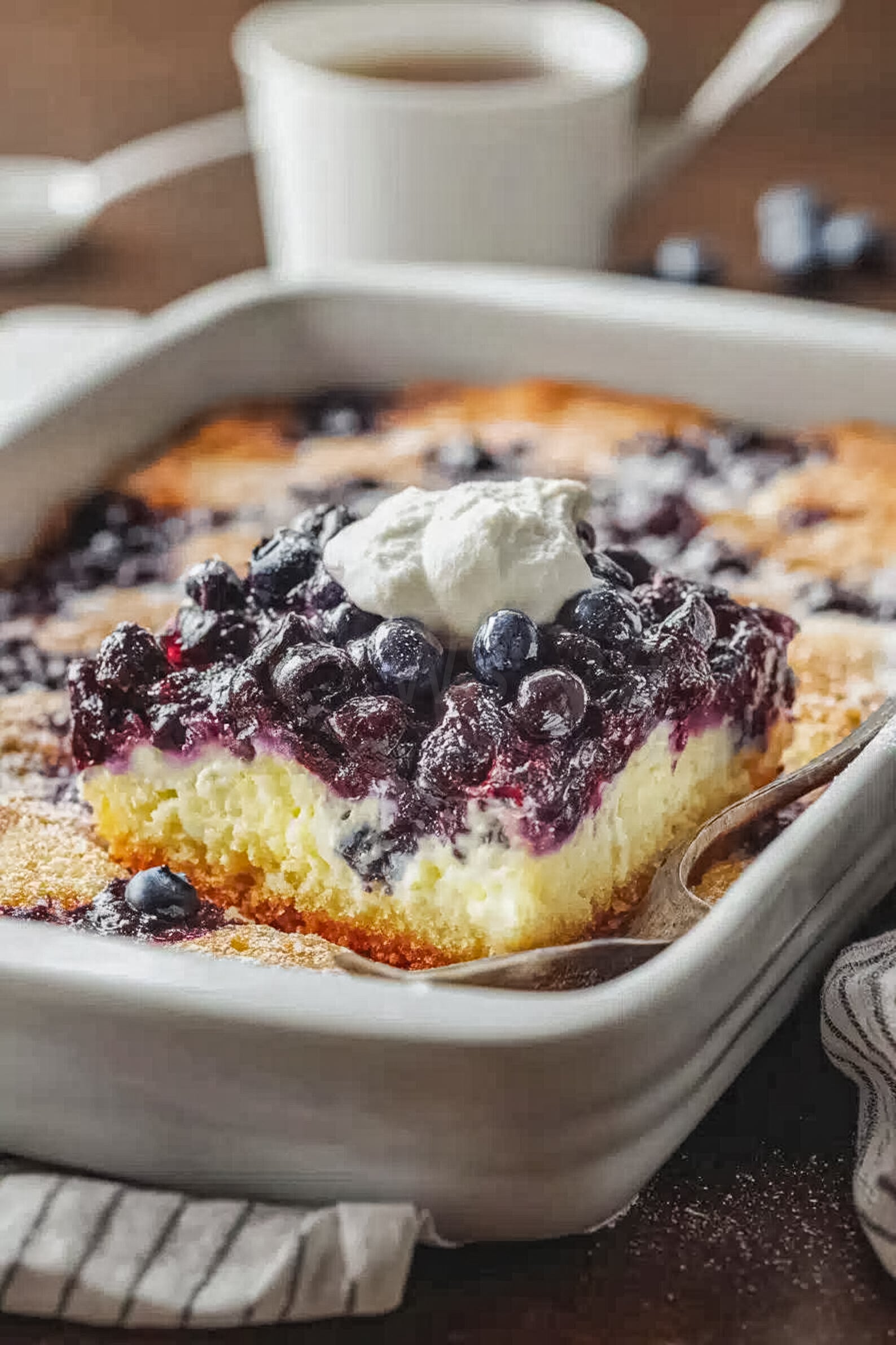 Blueberry lemon cheesecake dump cake served warm in a baking dish, topped with whipped cream and extra blueberries, showing creamy layers and juicy berry filling.