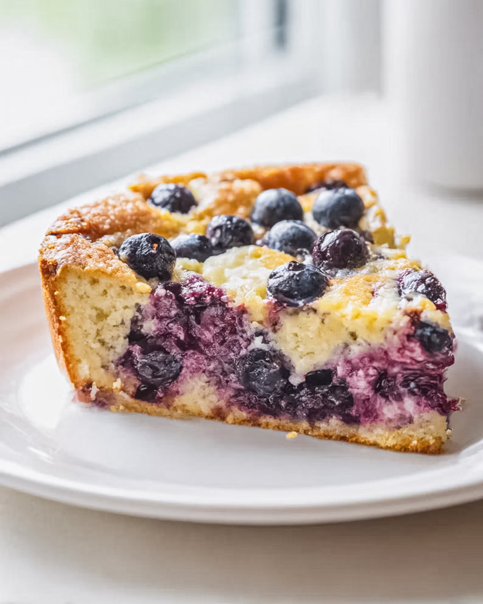 Blueberry lemon cheesecake dessert slice on a plate, topped with fresh blueberries, showing creamy filling, buttery cake, and juicy berry layers.