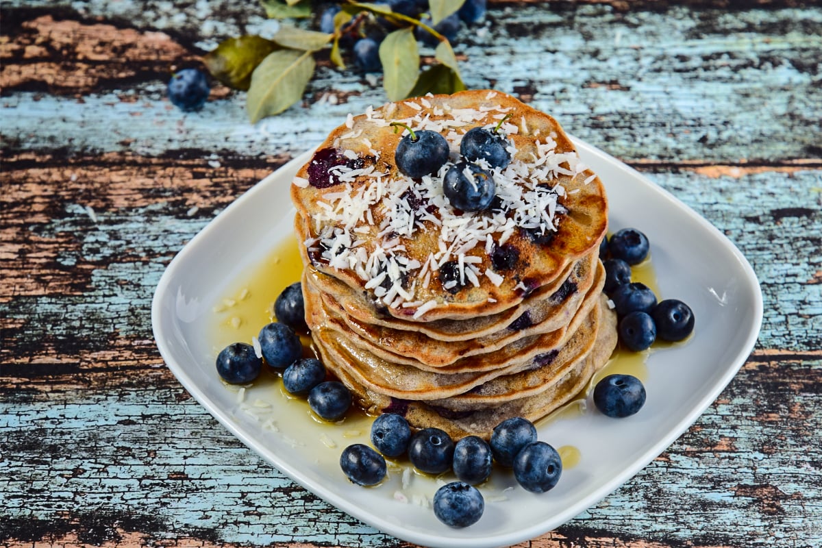 Soft gluten free coconut pancakes with juicy blueberries and golden edges, topped with extra berries.