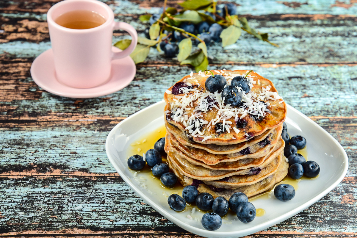 Golden blueberry coconut pancakes on a breakfast plate with fresh berries and a light coconut topping.