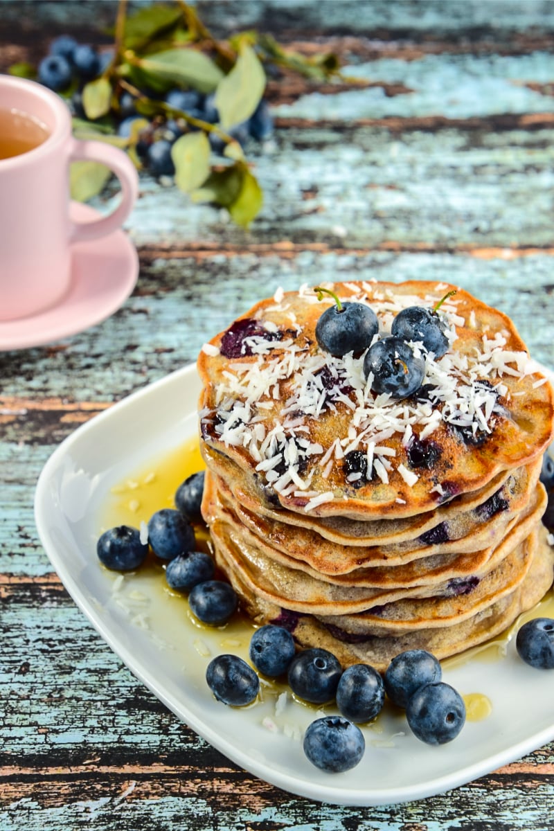 Close-up of fluffy gluten free pancakes filled with blueberries and shredded coconut, served warm with syrup.