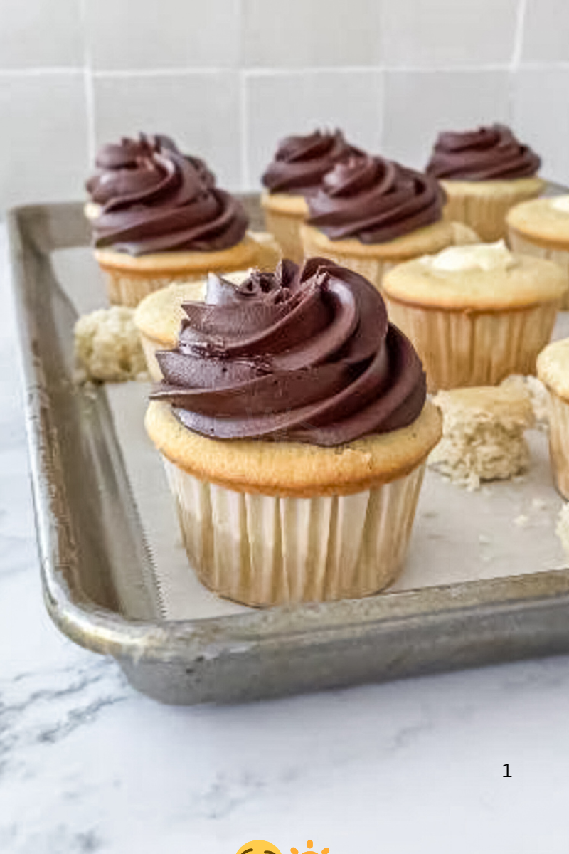 Boston Cream Cupcakes on a baking sheet, some topped with glossy chocolate swirls and others cored or filled with pastry cream before the final toppin