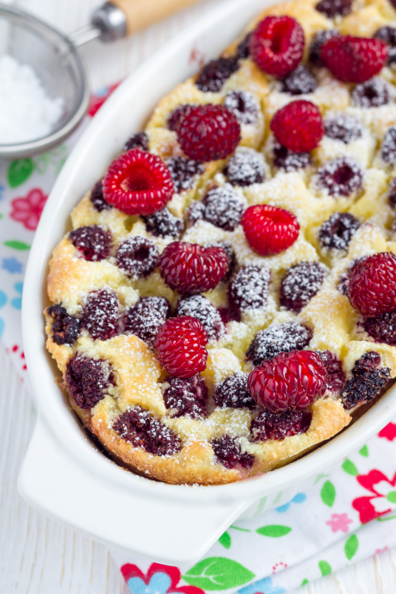Cottage cheese and raspberry semolina bake topped with fresh raspberries and powdered sugar in a baking dish, shown in a close-up view.