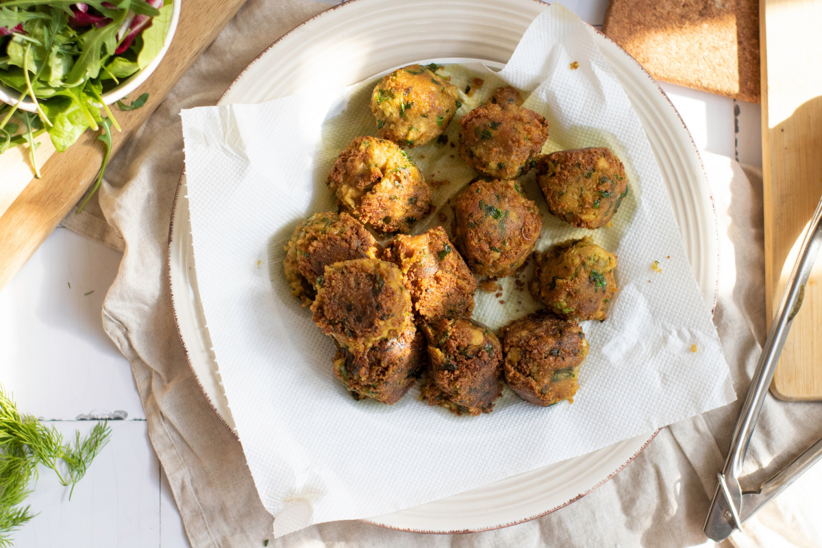Crispy falafel wrap being assembled with tzatziki, pickled onions, pickled radishes, cherry tomatoes, greens, feta, and fresh herbs.