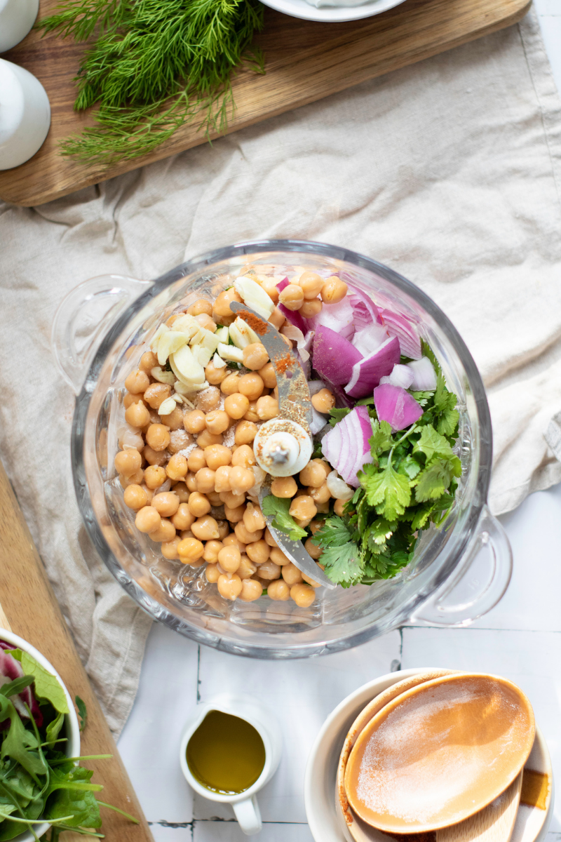 Chickpeas, red onion, garlic, fresh herbs, flour, and spices added to a food processor for homemade crispy falafel wraps.