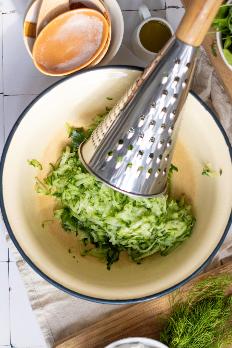 Fresh cucumber grated into a bowl for homemade tzatziki sauce with Greek yogurt, lemon, garlic, dill, and olive oil.