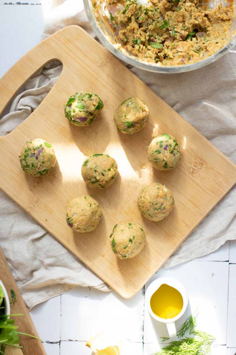 Homemade falafel mixture shaped into small balls on a wooden board before pan frying for crispy falafel wraps.