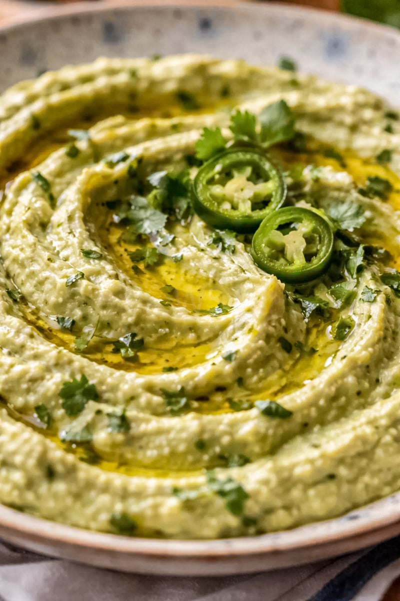 Creamy jalapeño hummus with a smooth swirled texture, topped with sliced jalapeños, chopped cilantro, and olive oil in a close-up overhead view.