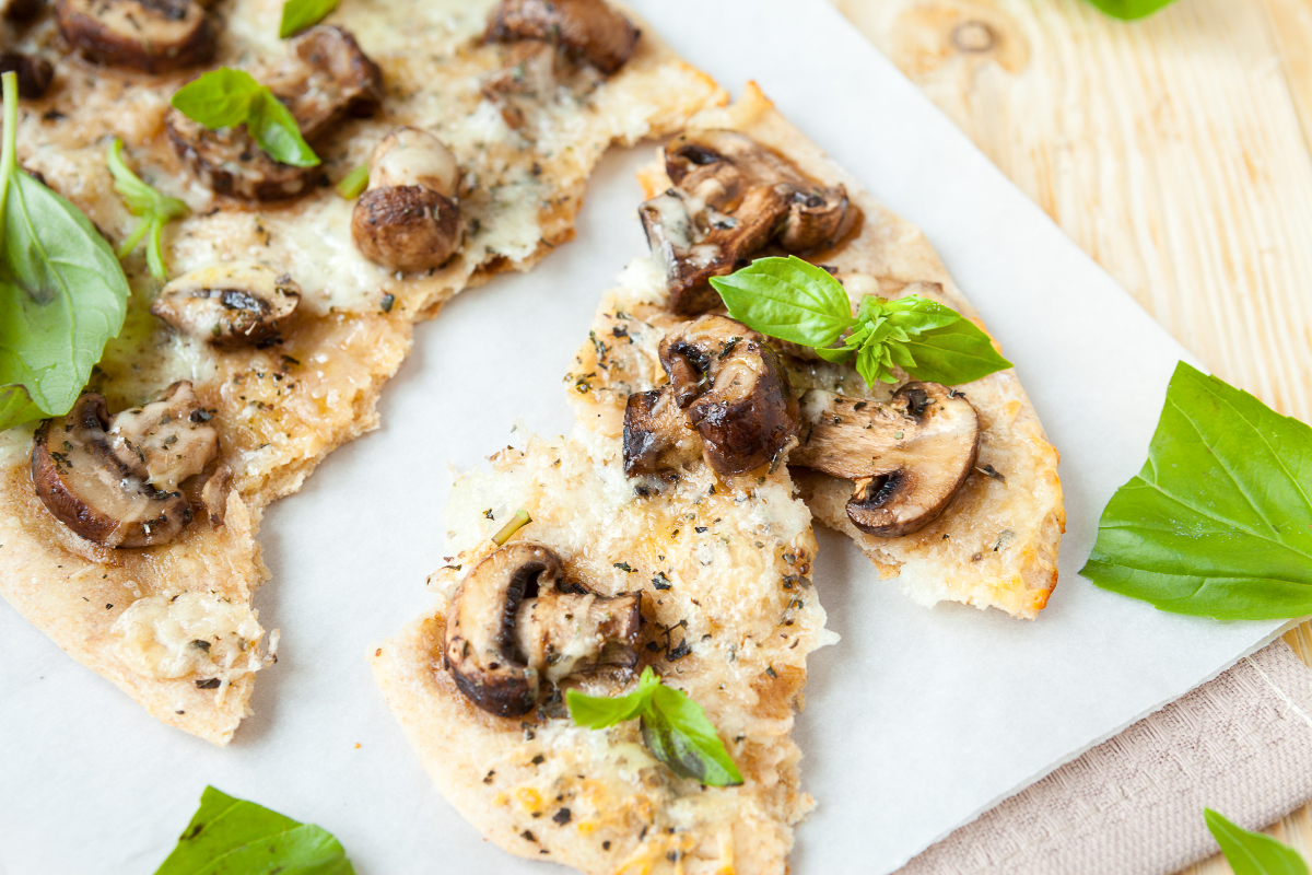 Sliced mushroom mozzarella pita flatbread with crispy edges, melted cheese, browned mushrooms, dried herbs, and fresh basil leaves ready to serve.