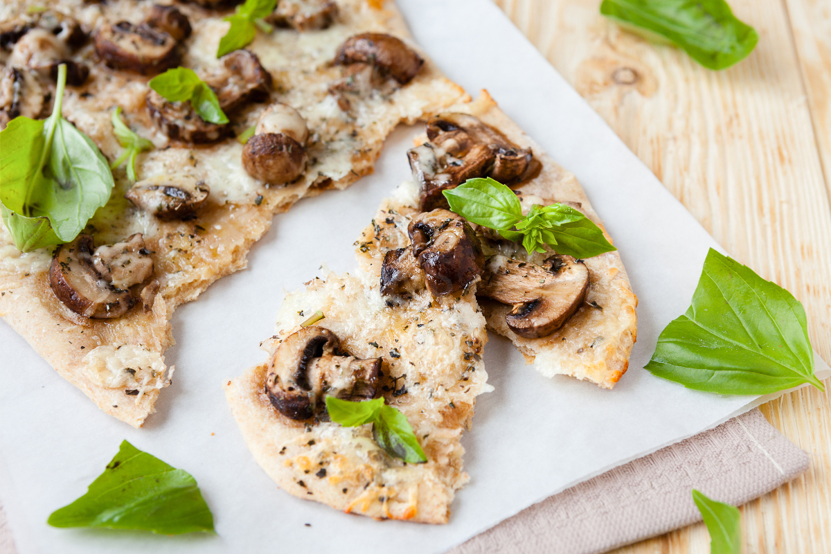 Mushroom mozzarella pita flatbread sliced into wedges with crispy pita edges, melted cheese, sautéed mushrooms, herbs, and fresh basil on parchment paper.