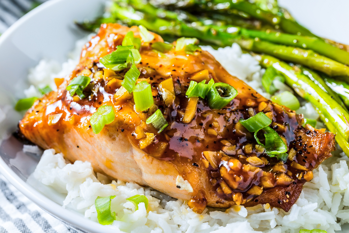 Baked teriyaki salmon served over white rice with roasted asparagus and topped with glossy teriyaki sauce, garlic, and green onions
