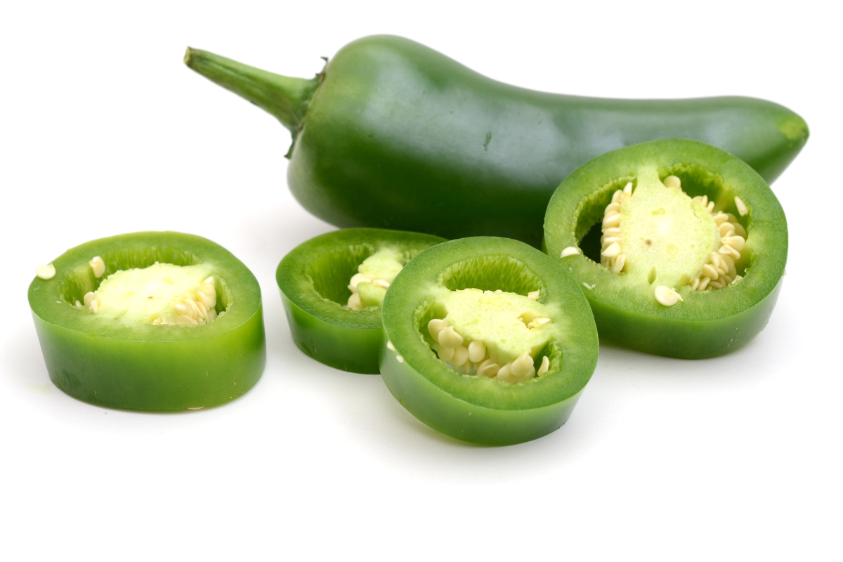 Whole jalapeño pepper with several sliced rounds, showing the seeds and bright green interior.