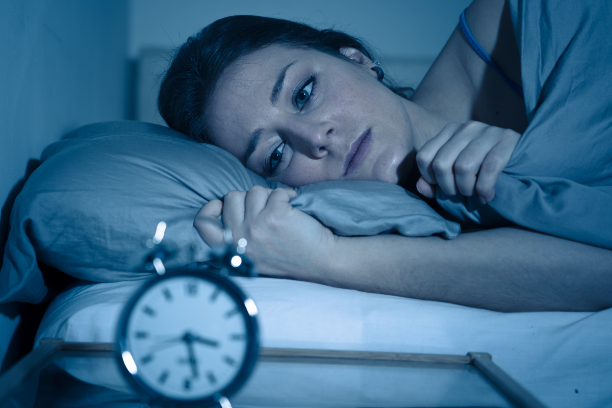Woman lying awake in bed at night with a blurred alarm clock in the foreground, illustrating insomnia, nighttime anxiety, and waking up in the middle of the night.