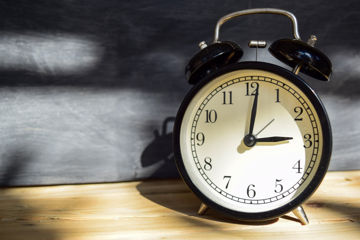 Alarm clock showing 3:00 on a wooden surface with a dark blurred background, illustrating middle-of-the-night waking and sleep interruption.