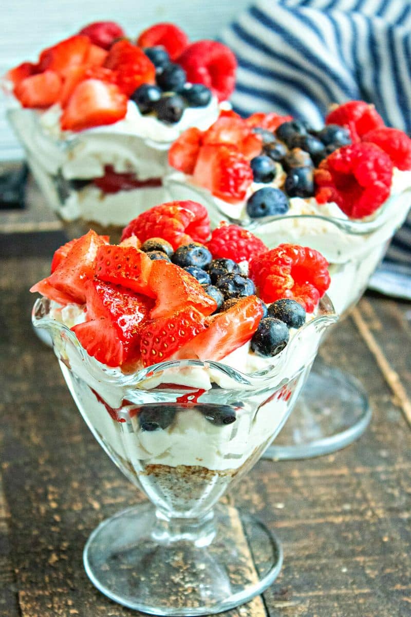 Greek yogurt berry cheesecake parfaits layered with whipped filling, strawberries, raspberries, and blueberries in glass dessert cups, shown in a close-up view.