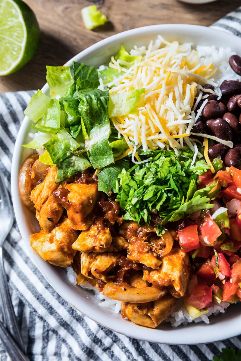 High protein chicken burrito bowl with seasoned chicken, black beans, shredded cheese, chopped romaine, cilantro, pico de gallo, and white rice in a close-up overhead view.
