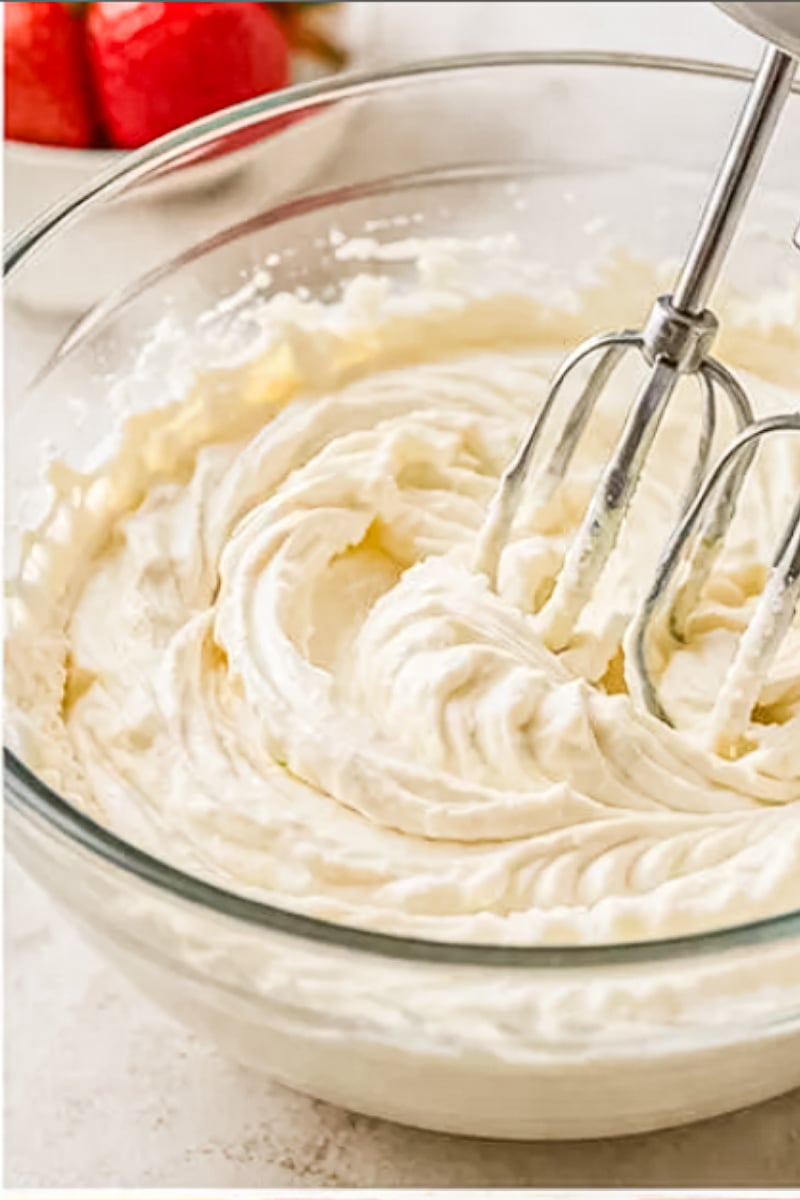 Creamy cheesecake filling being mixed with hand beaters in a glass bowl for mini no-bake berry cheesecakes.