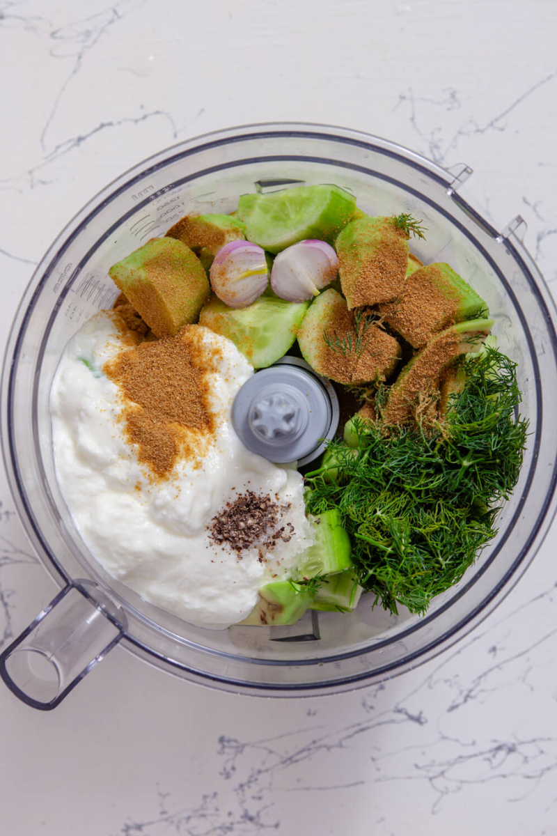 Cucumber, avocado, Greek yogurt, dill, lime juice, cumin, and shallot added to a food processor before blending soup.