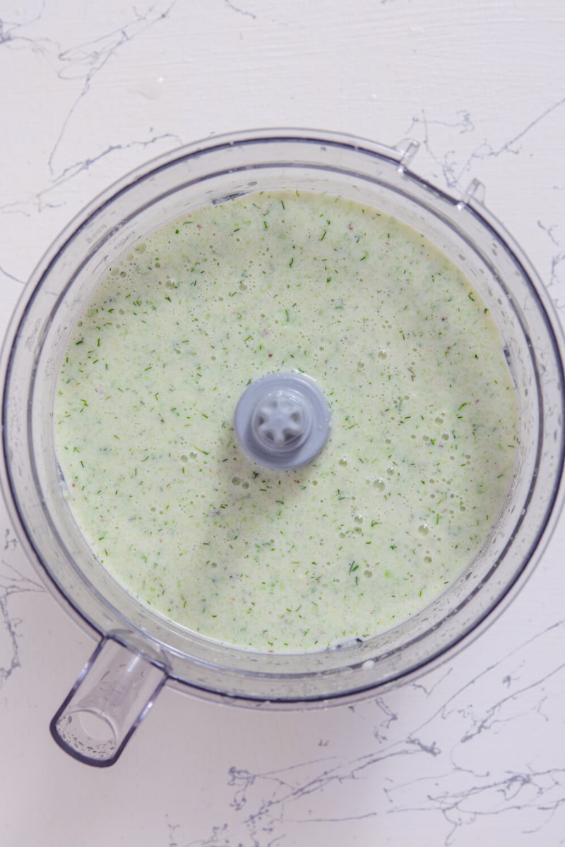 Creamy blended chilled cucumber avocado soup inside a food processor after mixing ingredients until smooth.