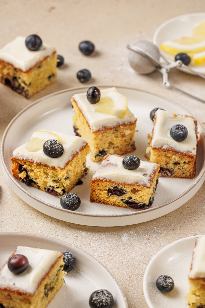 Lemon blueberry cake squares with cream cheese frosting, fresh blueberries, and lemon slices arranged on a serving plate.