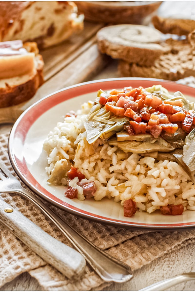 Close-up dinner plate with tender artichokes, crisp bacon pieces, and creamy rice.