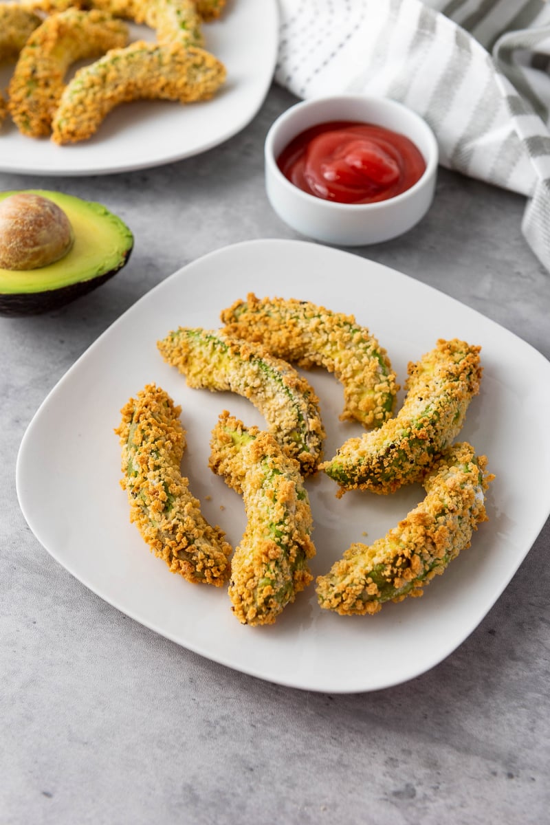 Crispy vegan air fryer avocado fries with golden panko coating, creamy avocado centers, and red dipping sauce served on a white plate for an easy appetizer or snack.