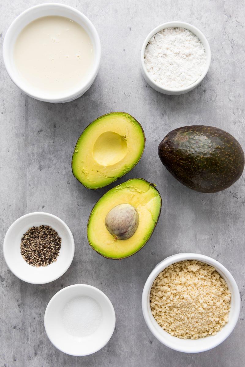 Ingredients for vegan air fryer avocado fries including avocado, soy milk, flour, breadcrumbs, salt, and pepper on a marble surface