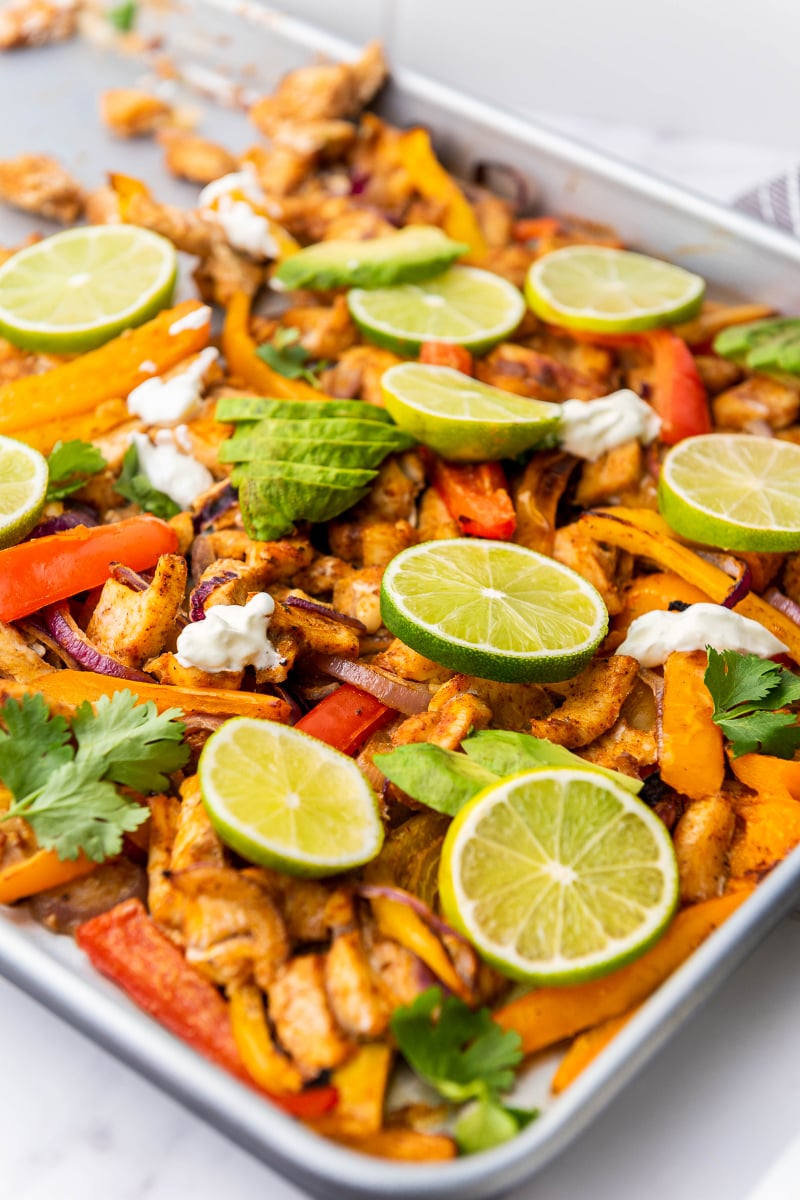 Colorful sheet pan chicken fajitas with seasoned chicken, roasted bell peppers, onions, warm tortillas, avocado, lime, and fresh toppings.