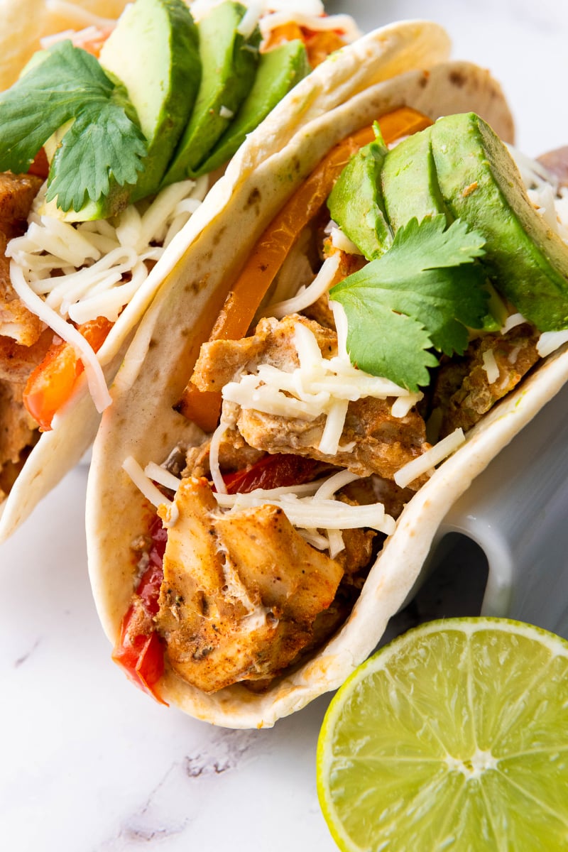 Sheet pan chicken fajitas served in warm tortillas with roasted peppers, onions, avocado, cheese, sour cream, cilantro, and fresh lime.