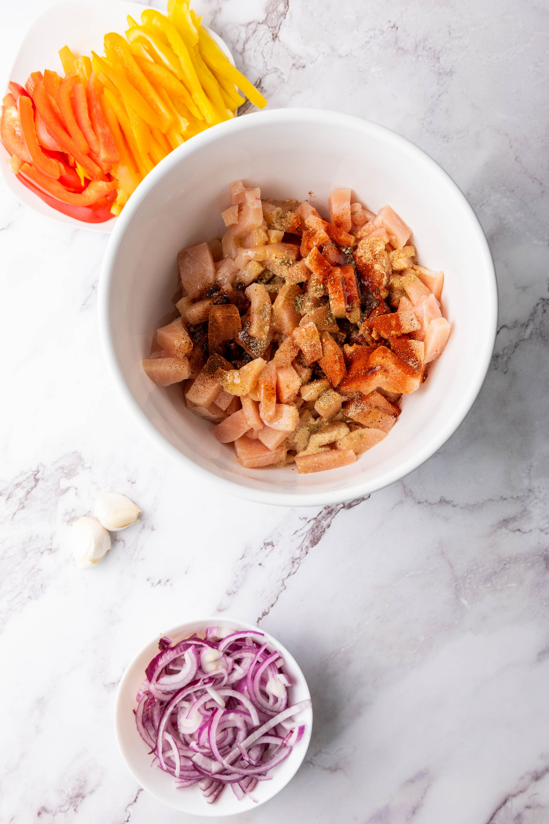 Diced chicken seasoned with olive oil, garlic, paprika, cumin, chili powder, oregano, salt, and pepper for homemade sheet pan fajitas.