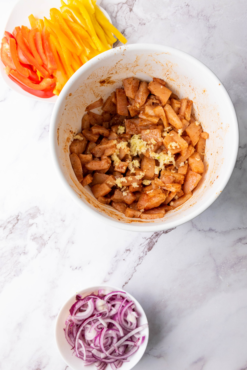 Seasoned chicken mixed with sliced bell peppers and red onions before baking for easy sheet pan chicken fajitas.