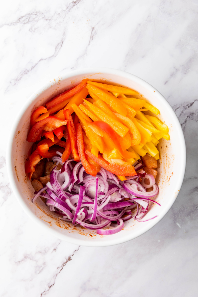Chicken, bell peppers, and onions spread in an even layer on a sheet pan before roasting for homemade chicken fajitas.