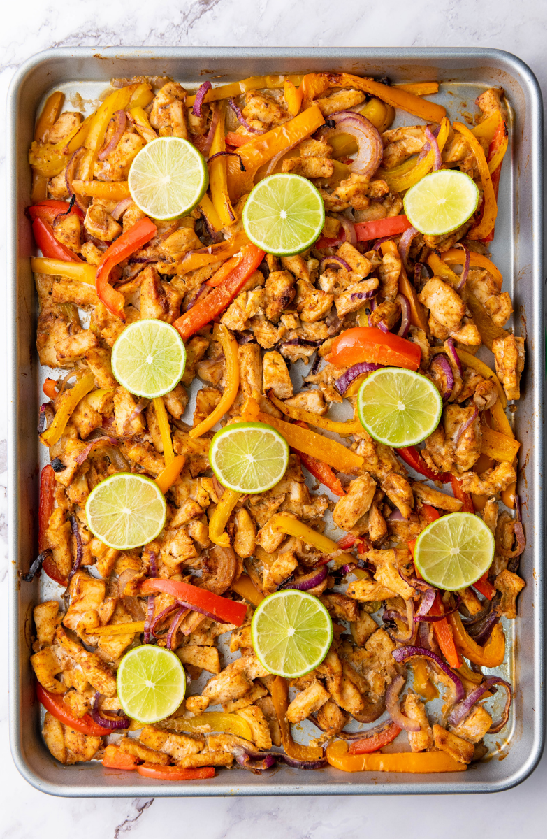 Warm tortillas arranged with roasted chicken fajitas, avocado, cheese, sour cream, lime, and cilantro for assembling fajitas.