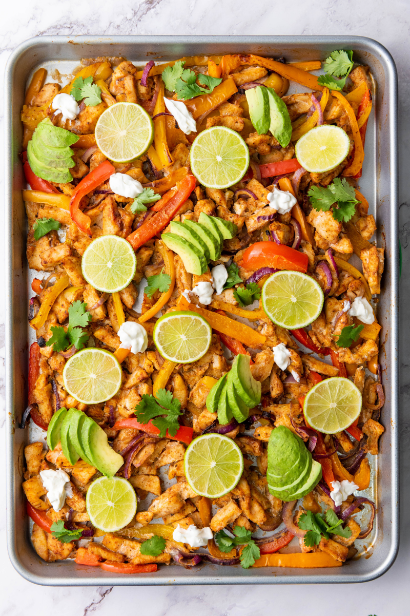 Assembled chicken fajitas in warm tortillas filled with roasted chicken, peppers, onions, avocado, cheese, sour cream, cilantro, and lime.