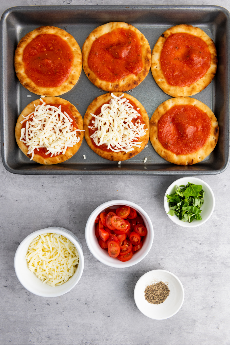 Mini naan pizzas topped with pizza sauce and shredded mozzarella cheese before adding tomatoes and baking in the oven.