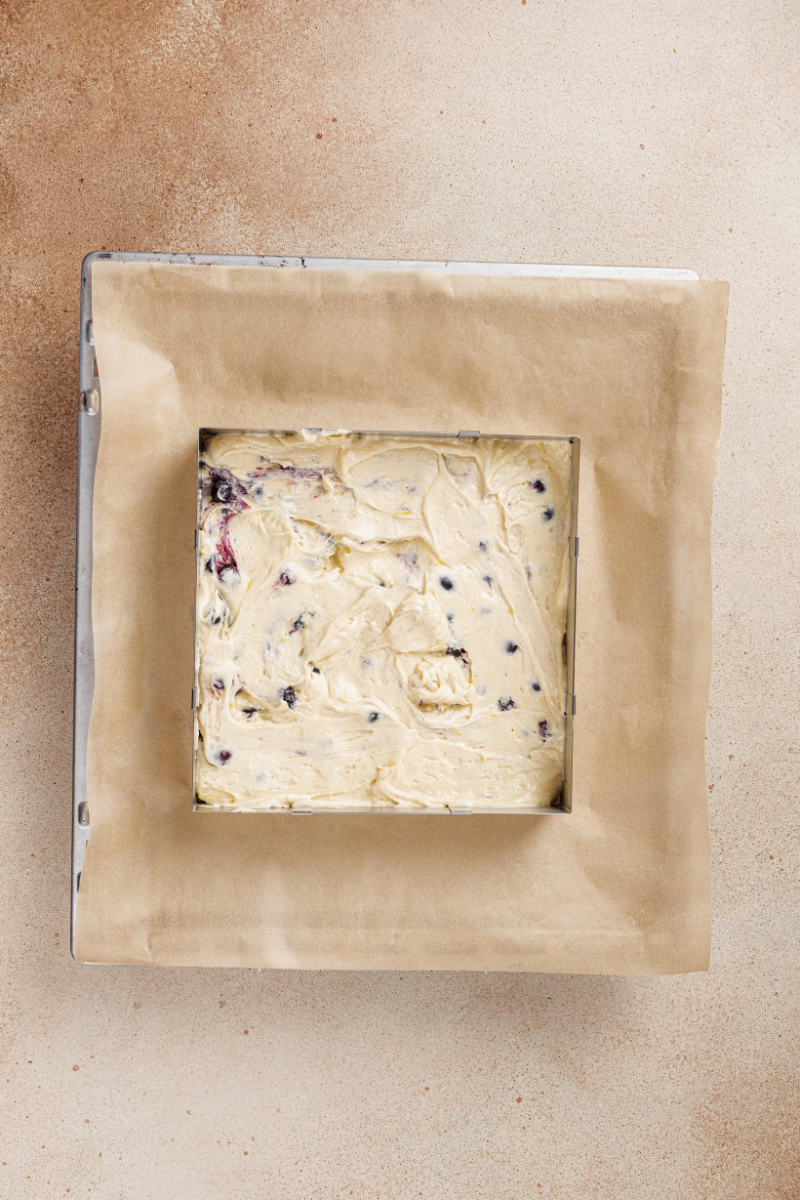 Lemon blueberry cake batter spread into a lined square baking pan before going into the oven.