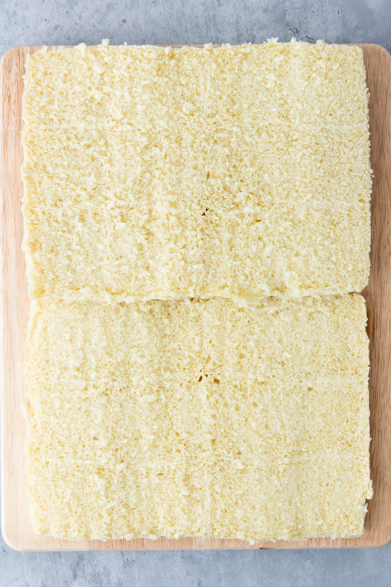 Slider buns sliced in half horizontally on a wooden board for baked ham and cheese sliders.