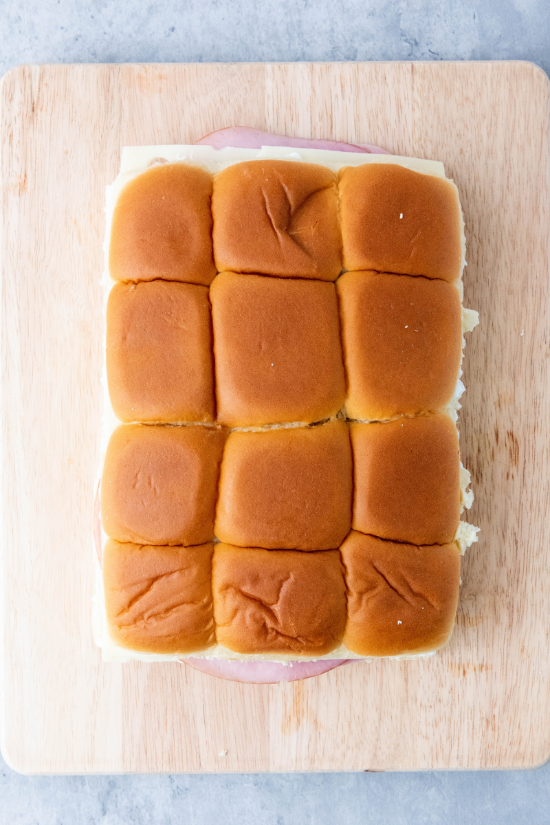 top buns placed over ham and Swiss cheese sliders before adding the buttery glaze.