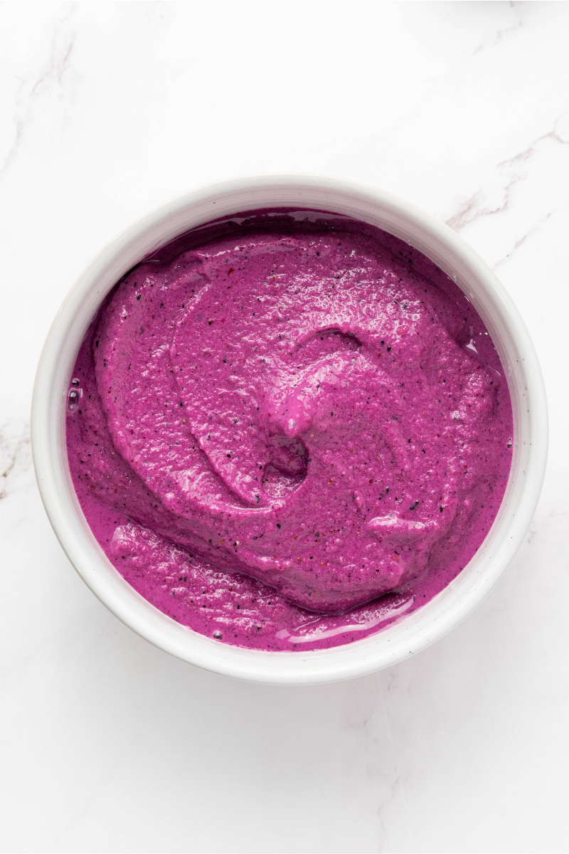 Thick purple smoothie base poured into a white bowl and smoothed into an even layer before adding toppings.