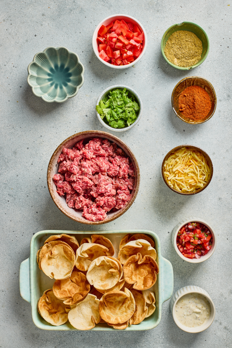 Ingredients for Taco Ranch Bites including ground beef, taco seasoning, shredded cheese, diced tomatoes, cilantro, and tortilla scoop chips.