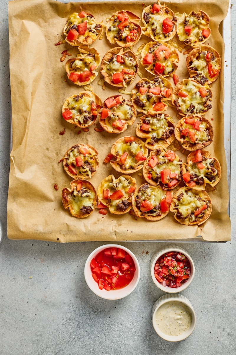  Baked taco ranch bites with melted cheese, diced tomatoes, and crispy tortilla cups served with salsa and creamy ranch sauce on the side.

